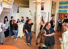 Junge Menschen und Erwachsene sprechen miteinander in einem Foyer mit Stehtischen und Bannern.