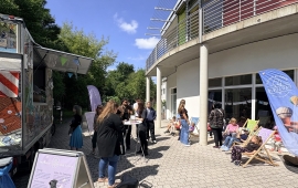 Vor einem Gebäude sitzen Menschen in Liegestühlen. Links im Bild ein Foodtruck.