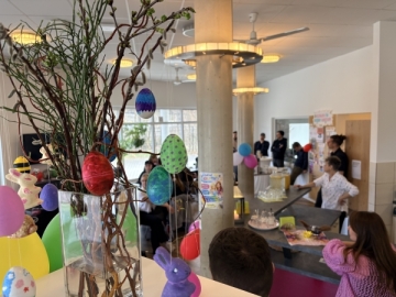 Im Vordergrund steht ein Strauß mit Ostereiern, im Hintergrund ein Raum mit Menschen, die essen und feiern.