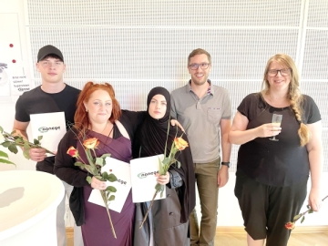 Drei junge Menschen und zwei Erwachsene stehen vor einer weißen Wand. Die Jugendlichen halten Rosen und ein Dokument in der Hand.
