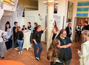 Junge Menschen und Erwachsene sprechen miteinander in einem Foyer mit Stehtischen und Bannern.
