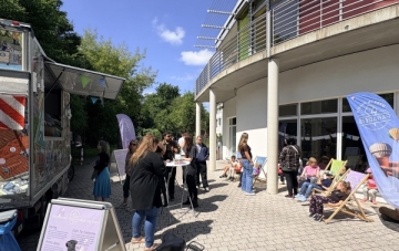 Vor einem Gebäude sitzen Menschen in Liegestühlen. Links im Bild ein Foodtruck.