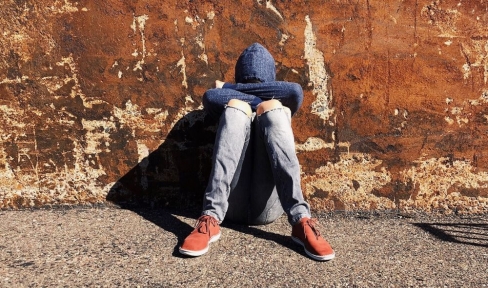 Jugendlicher mit Hoodie über dem Kopf sitzt deprimiert an Hauswand 
